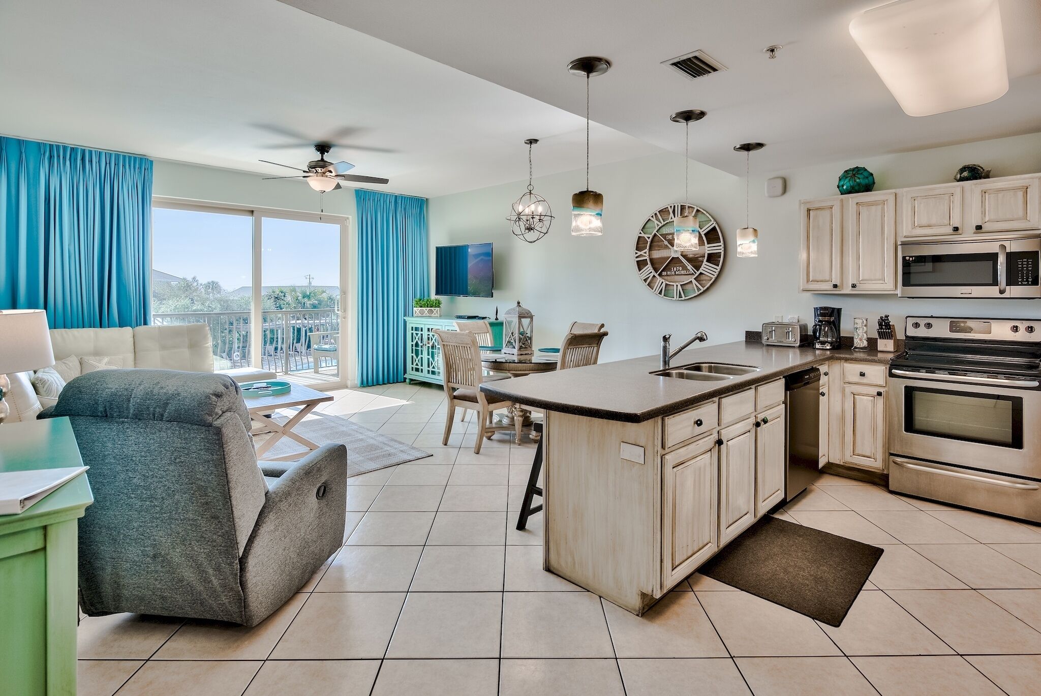 A modern kitchen with a central island, a dining area with a table and chairs, and a living room with a sofa and a view of the outdoors.