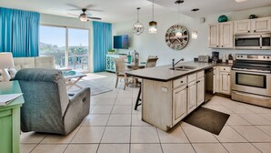 A modern kitchen with a central island, a dining area with a table and chairs, and a living room with a sofa and a view of the outdoors. - Relax and Enjoy Gulf Views & Excellent Pools, 3rd floor, Garage Parking (Miramar Beach)