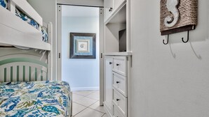 Une chambre avec un lit superposé, une commode et une porte donnant sur une autre pièce.