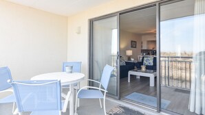 A balcony with a glass door leading to a living area with a sofa, coffee table, and lamp. - Direct Oceanfront, Mid-Town, Updated & Spacious 1st Floor - Walk off to Beach (Ocean City)