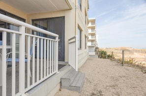 A beachfront hotel with a balcony, steps leading to the entrance, and a sandy beach in the background.