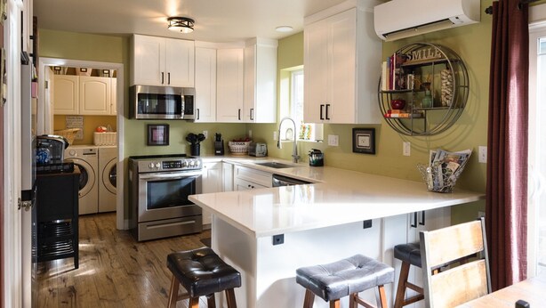 Une cuisine moderne avec des meubles blancs, des appareils en acier inoxydable et un îlot central doté de tabourets de bar.