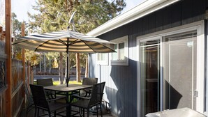 Une terrasse extérieure avec une table et des chaises, un parasol à rayures et une porte-fenêtre coulissante.