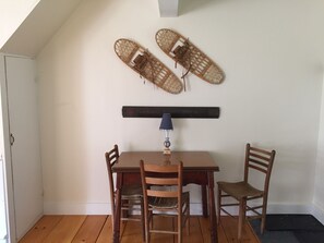 A dining area with a wooden table and chairs, a wall-mounted lamp, and two wall-mounted baskets. - In town, river across the street, families welcome (Waitsfield)