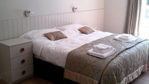 Ein ordentlich bezogenes Bett mit einer gesteppten Decke, ein Nachttisch mit Schubladen und drei gerahmte Bilder an der Wand.