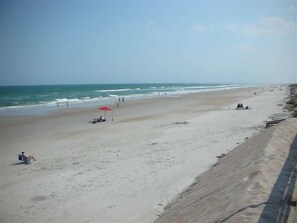 A beach with a few people, a red umbrella, and a sandy shore.