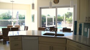 A kitchen with a large island, white cabinets, and a view of a swimming pool outside. -  Beautiful Home in Key Colony Beach! Private Pool. Dock. Tiki Hut (Key Colony Beach)