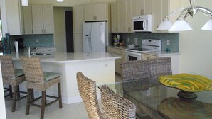 A kitchen with white cabinets, a white refrigerator, a microwave, and a stove. There are wicker chairs and a glass table with a decorative plate. -  Beautiful Home in Key Colony Beach! Private Pool. Dock. Tiki Hut (Key Colony Beach)