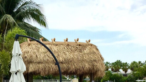 A pool area with a thatched-roof structure, lounge chairs, and a view of boats on the water. -  Beautiful Home in Key Colony Beach! Private Pool. Dock. Tiki Hut (Key Colony Beach)