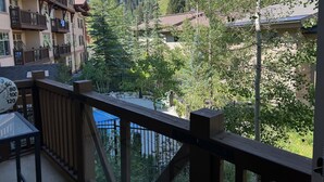 Un balcon doté d’une balustrade en bois, donnant sur une région montagneuse parsemée de bâtiments et d’arbres.