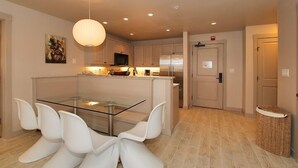 Une cuisine moderne avec une table à manger en verre et des chaises blanches, un luminaire suspendu et une porte avec une enseigne.