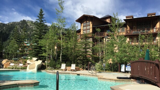 Un espace piscine doté d’un toboggan, de chaises longues et d’un bâtiment en bois avec des balcons.