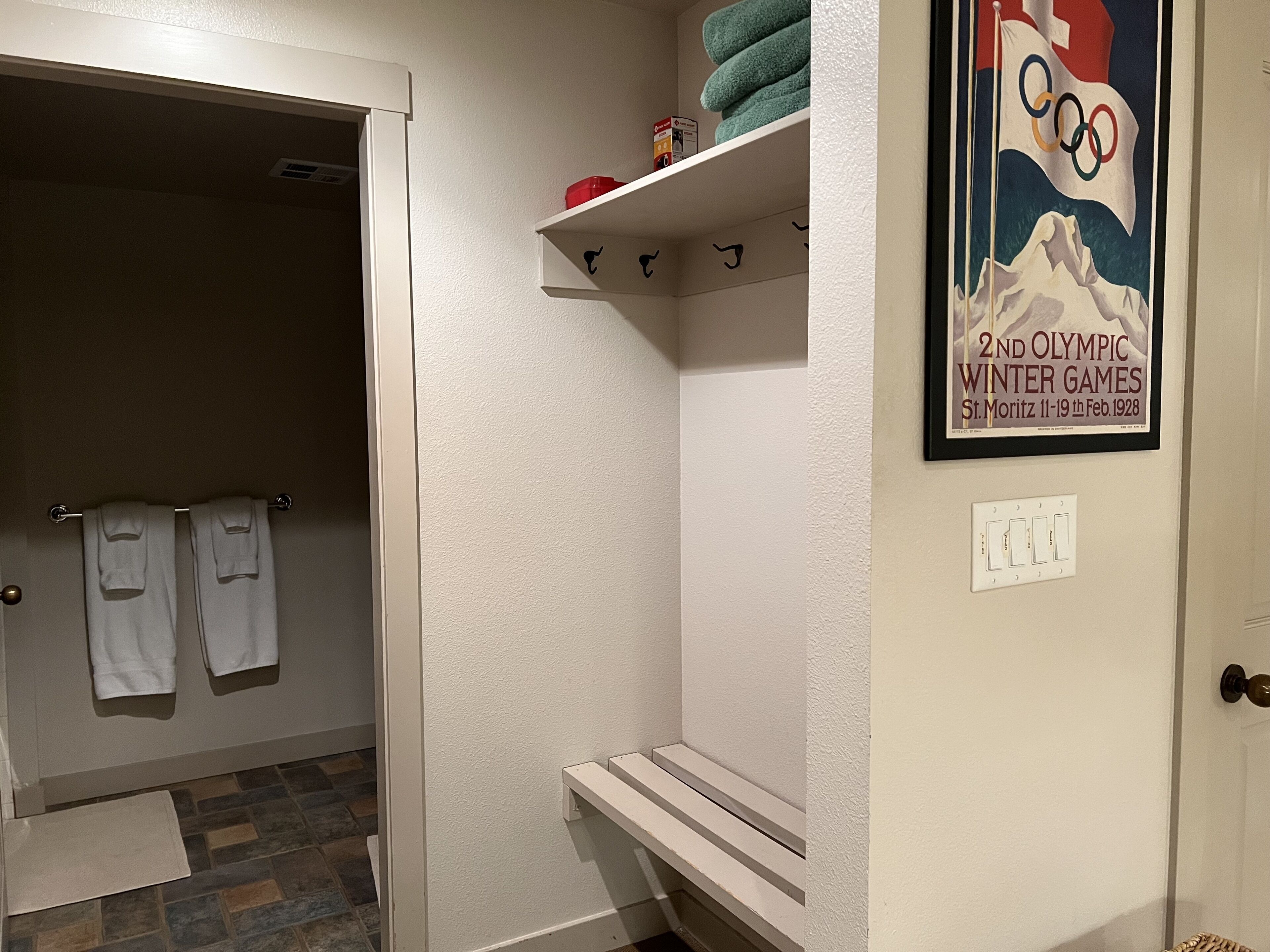 Un baño con ducha, un perchero con dos toallas, un estante con toallas y un objeto pequeño, y un cartel enmarcado en la pared.