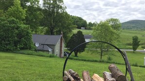 Un paysage rural avec une maison, un porte-bois en métal et un champ d’herbe.