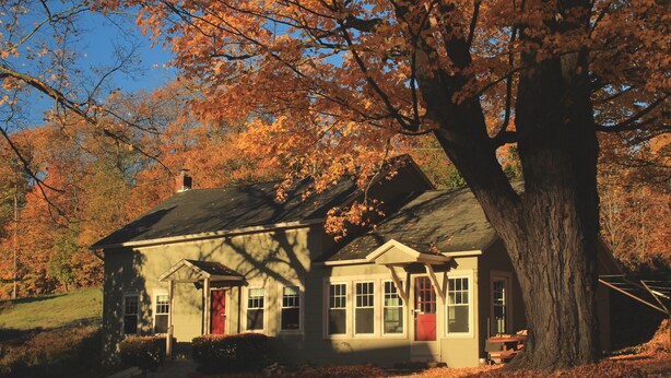 Une maison avec une porte rouge, un porche et un grand arbre devant.