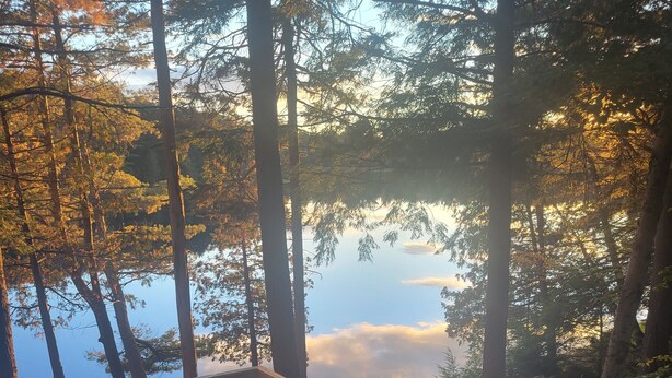 A wooden deck overlooking a forested area with a view of a lake. - Riverside 3 bedroom 2 bath near Baxter State Park (Millinocket)