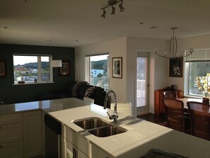 A modern kitchen with a large island, a built-in dishwasher, and a dining area with wicker chairs. - 2 Bedroom Apt RIVER & MOUNTAIN VIEWS , IN THE HEART OF WHITEHORSE - condo (Whitehorse)