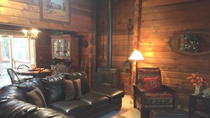 A cozy cabin interior with a leather sofa, a dining table, and a fireplace.