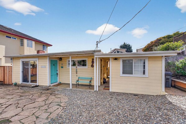 A small, single-story building with a front porch, a turquoise door, and a bench. - Coastal Breeze Cottage (Aptos)