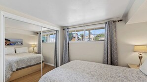 Un dormitorio con una cama grande, una cama más pequeña, una ventana con cortinas y un cuadro en la pared.