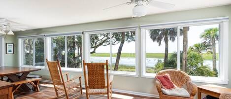 A spacious room with a large dining table, two rocking chairs, a wicker sofa, and a ceiling fan.