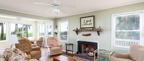 A living room with a fireplace, two armchairs, a sofa, and a ceiling fan.
