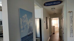 A hallway with a 'Beach House' sign, a refrigerator, and a painting of a sailboat on the wall.