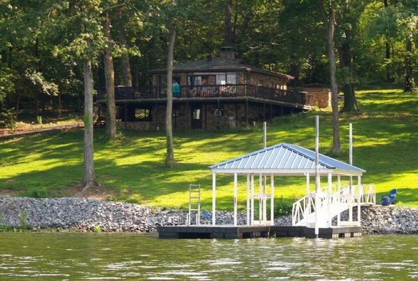 A lakeside lodge with a dock, a covered pavilion, and a stone house in the background.