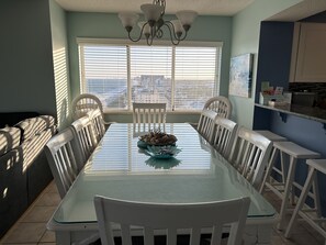 A dining area with a glass table, white chairs, and a view of the city through large windows.