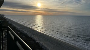 En strand med solnedgang, klar himmel og en fjerntliggende bysilhuet.