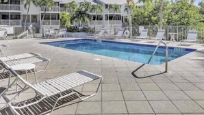 A pool area with lounge chairs, a pool, and a building with balconies. - Florida Keys Townhouse For Rent 2/2 (Key Largo)
