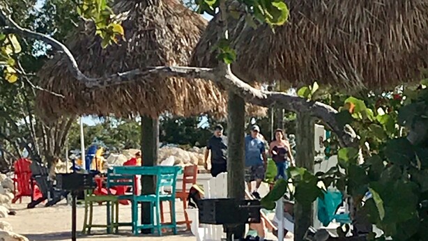 A beach area with thatched umbrellas, a table with chairs, and rocky terrain. - Florida Keys Townhouse For Rent 2/2 (Key Largo)