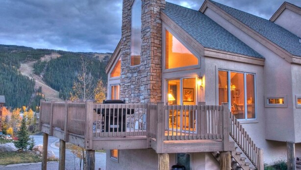 A two-story house with a stone chimney, large windows, and a wooden deck. - 5BR+Loft BR Home in Keystone Ski Area-pvt. hot tub; great view; 16 separate beds (Keystone)