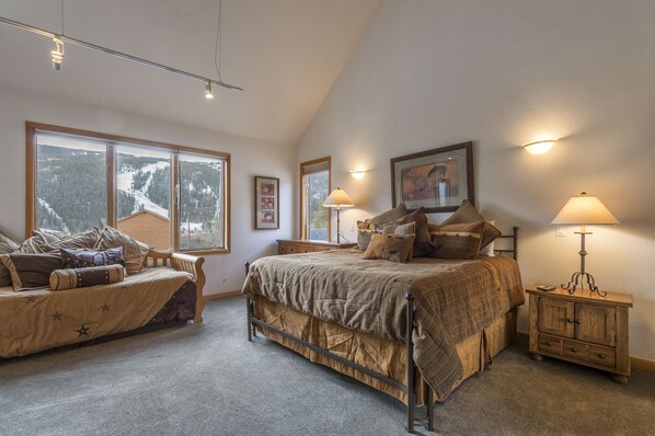 A bedroom with a large bed, a chair, a nightstand, and a window with a view of a snowy mountain. - 5BR+Loft BR Home in Keystone Ski Area-pvt. hot tub; great view; 16 separate beds (Keystone)