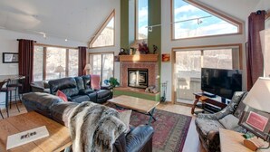 A spacious living room with a fireplace, large windows, a television, and a cozy seating area. - 5BR+Loft BR Home in Keystone Ski Area-pvt. hot tub; great view; 16 separate beds (Keystone)
