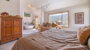 A bedroom with a large bed, a wooden cabinet, a bathtub, and a window with a view of the outdoors. - 5BR+Loft BR Home in Keystone Ski Area-pvt. hot tub; great view; 16 separate beds (Keystone)