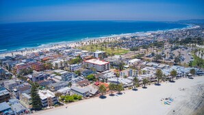 Vista aérea de uma cidade costeira com praia, edifícios e céu azul límpido.