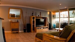 Uma sala de estar com um móvel de entretenimento de madeira, televisão, sofá e um espaço de refeições com mesa e cadeiras.