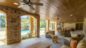 A covered outdoor area with stone walls, a wooden table, wicker furniture, and ceiling fans. - Lake Palestine's Best Property for Vacations, Reunions, Events, Get-Aways!!! (Frankston)