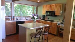 A kitchen with wooden cabinets, a dishwasher, a stove, and a coffee maker. There are two bar stools and a vase with flowers on the island.