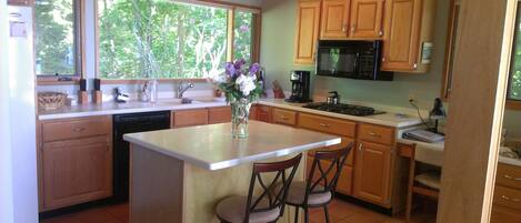 A kitchen with wooden cabinets, a dishwasher, a stove, and a coffee maker. There are two bar stools and a vase with flowers on the island.