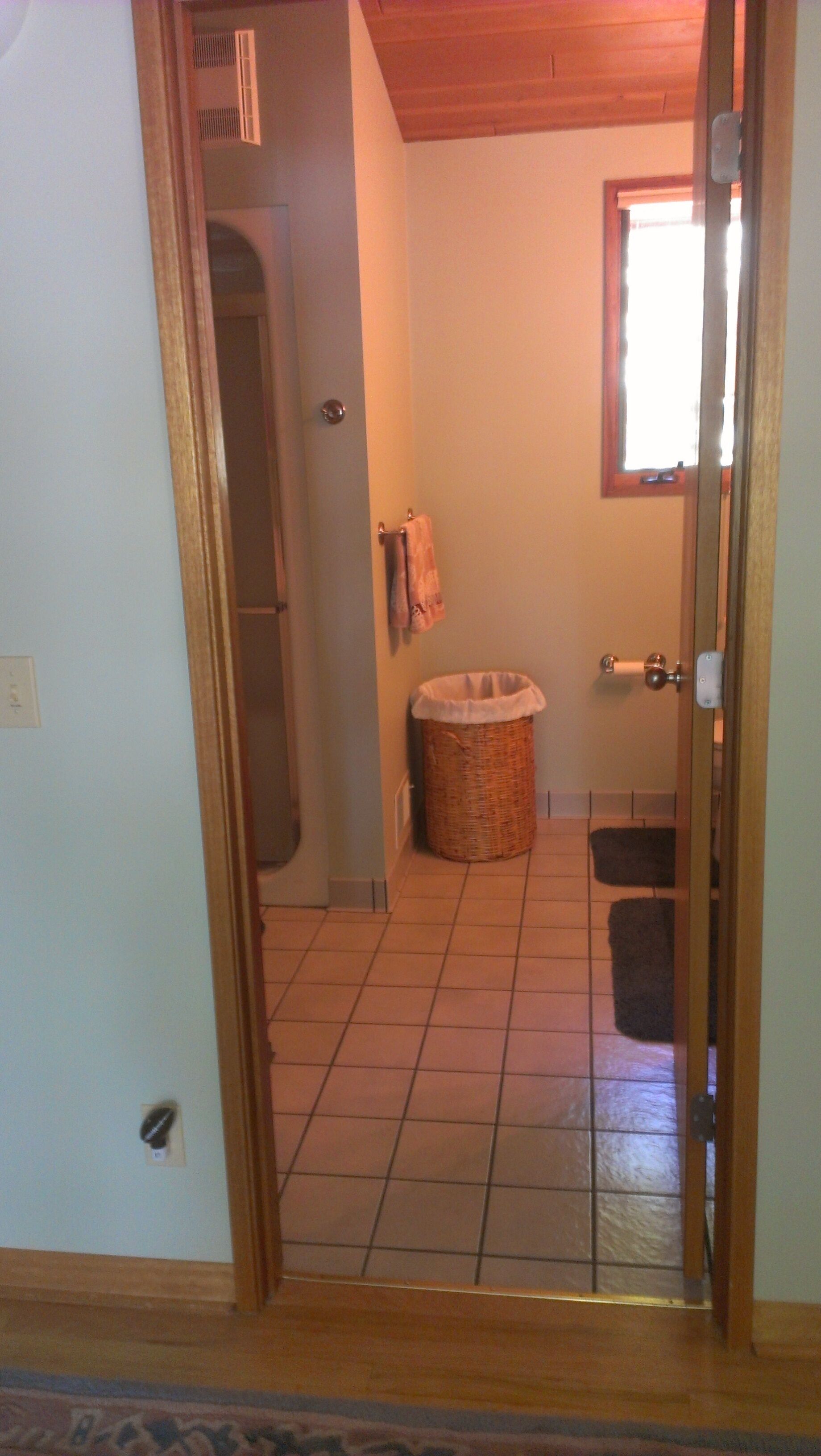 Un couloir menant à une salle de bain dont le sol est carrelé, où se trouvent un panier en osier et un porte-serviettes.