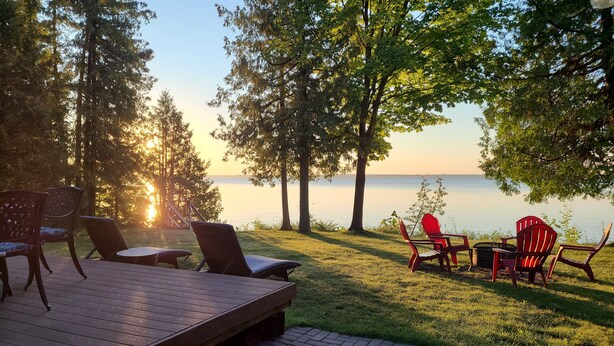 A deck with outdoor seating overlooking a lake, surrounded by trees.