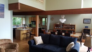 A spacious living area with a dark blue sofa, a wooden dining table, and a kitchen in the background.