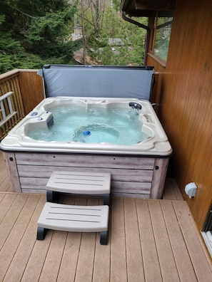A hot tub on a wooden deck with a view of trees.