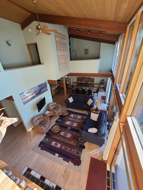 A spacious living area with a high ceiling, wooden beams, a large rug, and a dining area with chairs and a table.