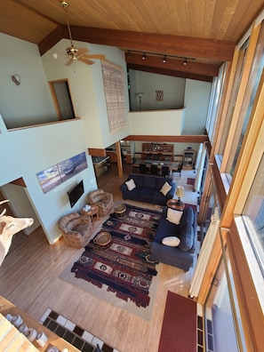 A spacious living area with a high ceiling, wooden beams, a large rug, and a dining area with chairs and a table. - Private Lakefront Suttons Bay Home with Hot Tub, Newly Renovated Beach and A/C! (Suttons Bay)