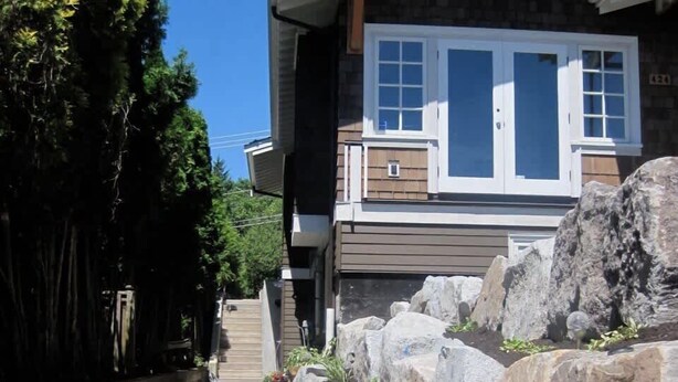 A pathway leading to a house with a stone retaining wall and large rocks.