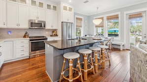 A modern kitchen with white cabinets, stainless steel appliances, a central island with stools, and a view of the outdoors.