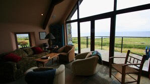 A living room with a view of the ocean, furnished with a sofa, chairs, and a table. - The Stone House - Wild Atlantic Way (Fanore)